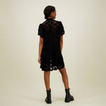 kuva mallista takaa päin jolla yllään naisten lyhyt musta pitsimekko frillahihoilla ja korkealla kauluksella, läpikuultava ilman aluspaitaa.