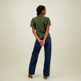 kuva takaa päin mallista jolla yllään naisten vihreä läpikuultava pitsitoppi korkealla kauluksella ja lyhyillä kerrostetuilla frillahihoilla.