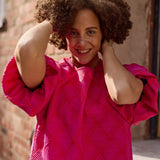 Lähikuva mallista jolla yllään naisten lyhyt jacquard-mekko oranssilla pohjalla ja pinkillä kuosilla, lyhyillä puhvihihoilla.