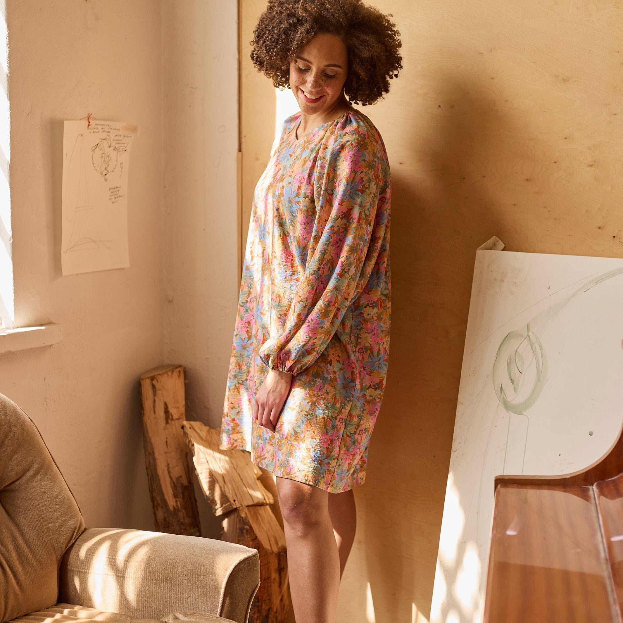 Naisten tunikamallinen viskoosimekko Cynthia De Vitin kuosilla, pitkät puhvihihat ja sivutaskut, malli seisoo nojaten seinään valon tullessa sivusta.