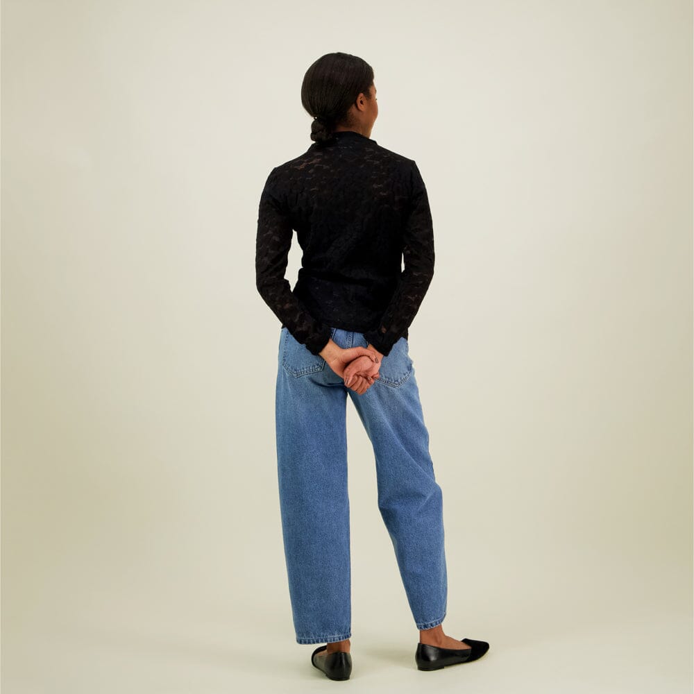 Naisten musta pitsipaita korkealla kauluksella ja pitkillä hihoilla, kuva mallista takaa päin. 