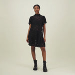 video jossa mallilla yllään musta lyhyt pitsimekko jossa frillahihat ja korkea kaulus.