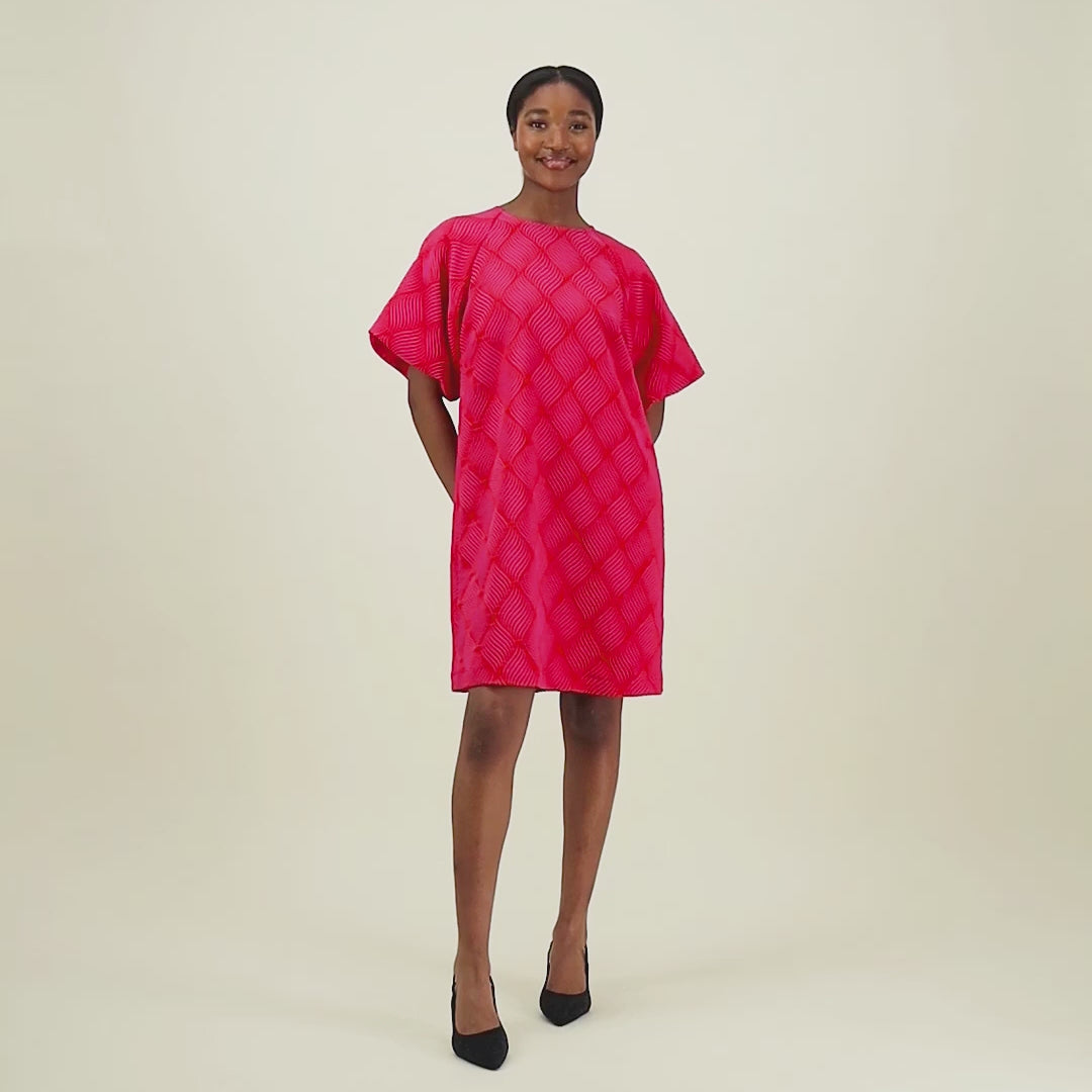 video jossa malli esittelee tuotteen lyhyt jacquard-mekko oranssilla pohjalla ja pinkillä kuosilla, lyhyillä puhvihihoilla.