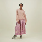 video, jossa nainen esittelee naisten midimittaisen purple-sävyisen laskostettu hame kierrätyspolyesterista, joustavalla vyötäröllä ja sivutaskuilla."