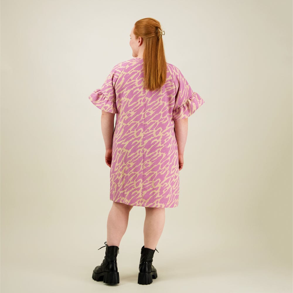 Naisten lyhyt suoralinjainen purple-sävyinen mekko kierrätyspolyesterista, frillahihoilla ja sivutaskuilla, kuva mallista takaa päin. 