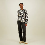 Naisten oversize-mallinen musta-ebige collegepaita pehmeästä luomupuuvillasta, harjattu sisäpinta, housut yhdistetty tummiin farkkuihin. 