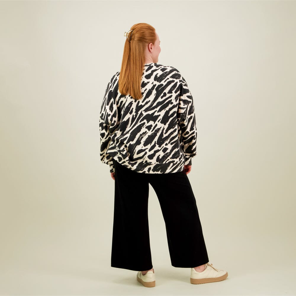 Naisten oversize-mallinen musta-beige collegepaita pehmeästä luomupuuvillasta, harjattu sisäpinta, kuva mallista takaa päin. 