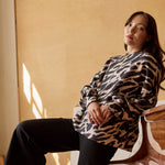 Malli nojaa pianoon yllään naisten oversize-mallinen musta collegepaita pehmeästä luomupuuvillasta, harjattu sisäpinta.