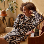 Nainen istuu pianoon nojaten päällään oversize-mallinen polvimittainen mustavalkoinen collegemekko sivutaskuilla.